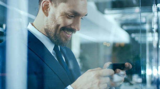 istock Handsome Businessman Standing in the Office Hallway Uses Smartphone, Smiling. 978271602