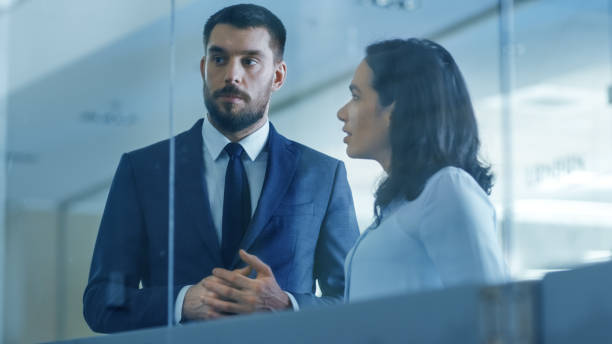 istock Top Manager and Female Executive Outlining Company Optimization Plan on a Glass Blackboard, Drawing with Market and Using Sticky Papers while Standing in the Modern Glass and Concrete Office. 978271624