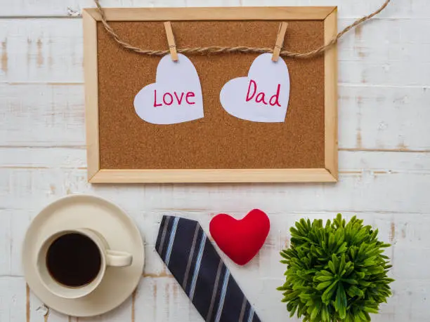 Happy Father's Day inscription with colorful tie, redheart, plant and a cup of coffee  on white wooden background.father's day concept.
