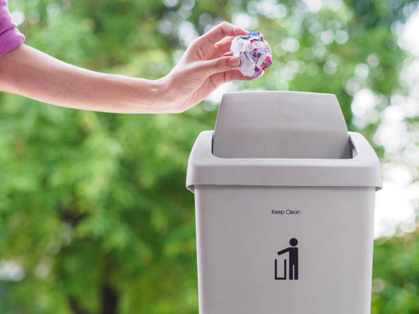 istock female hand trowing a paper into a garbage bin on bokeh background. cleaning concept. 978277326