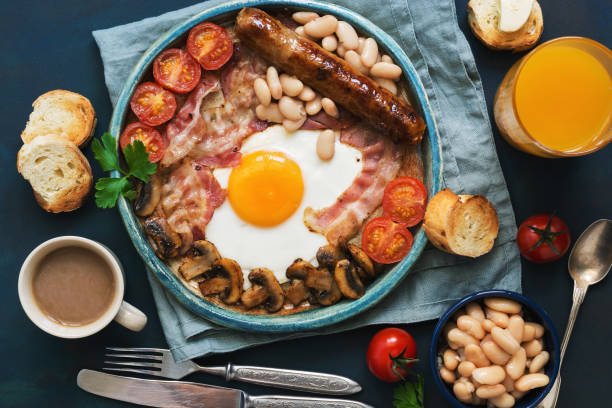 istock Traditional English breakfast. Fried egg with sausage, mushrooms, beans, tomatoes and bacon. View from above.Toast with butter, coffee and orange juice. 978320914