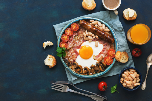 Traditional English breakfast on a blue background. Fried egg with sausage, mushrooms, beans, tomatoes and bacon. Top view, copy space