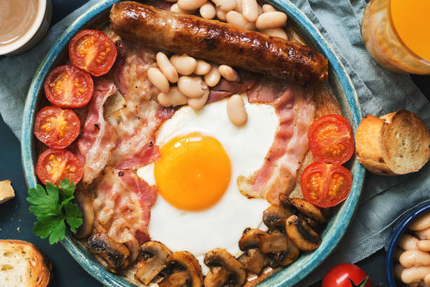 istock Traditional English breakfast close-up on a blue background, top view. Fried egg with sausage, mushrooms, beans, tomatoes and bacon 978321190