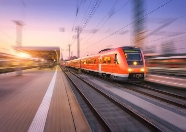 istock High speed red train with motion blur effect on the railway station at sunset. Landscape. Modern intercity passenger train in motion on the railway platform at dusk. Commuter vehicle on railroad 978321584