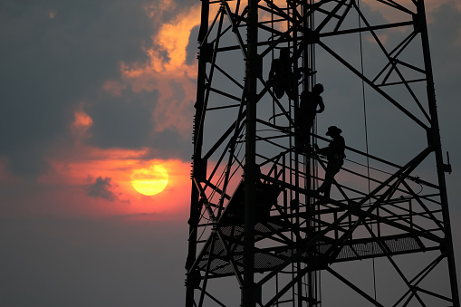 Workers are climbing to repair the telecommunication tower or poles, in the evening,Red sky sunset background