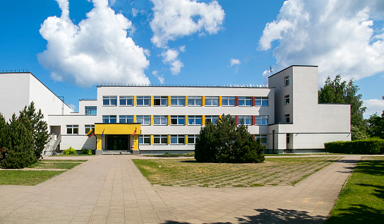 Public school building. Exterior view of school building with playground. Sunny sky with clouds