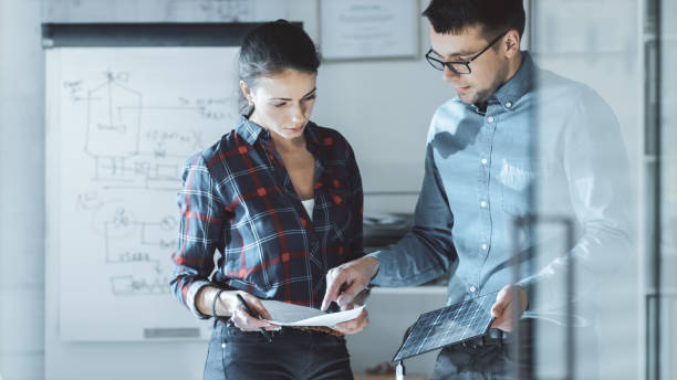 female design engineer works on documents in a conference room, last minute check-up, uses her smartphone. in the background whiteboard with schemes on it, various blueprints hanging on the walls. - applied science imagens e fotografias de stock