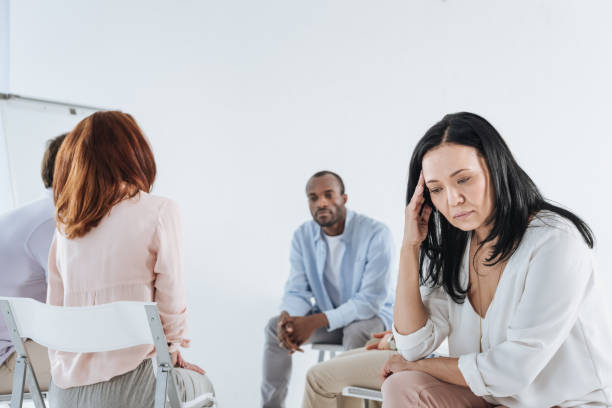 istock depressed asian woman looking down and multiethnic group sitting behind 978357272