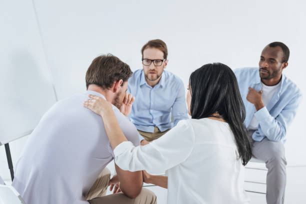 istock multiethnic mid adult people sitting on chairs and supporting upset man during anonymous group therapy 978363638