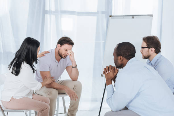 istock multiethnic middle aged people sitting on chairs and supporting upset man during anonymous group therapy 978363770