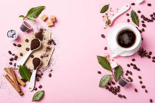 Food background with ground coffee in spoons, coffee beans, espresso cup, ground and capsules, green leaves, copy space, top view.
