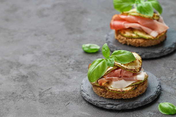 istock Mini ham  (hamon, prosciutto) sandwiches, fried zucchini and Basil close-up on black surface. Gourmet snack 978462450