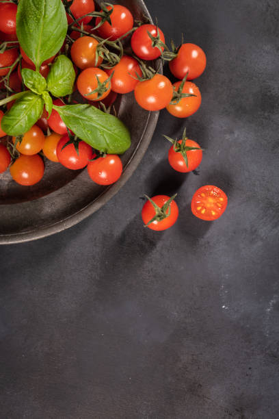 istock Small red cherry tomatoes on rustic background. Cherry tomatoes on the vine witb basil leaves 978470064
