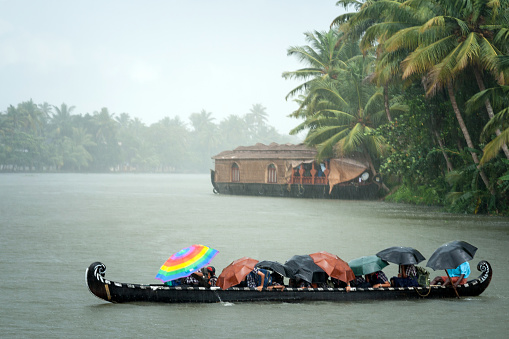 Monsoon time. People crossing a river by boat in rain with umbrellas