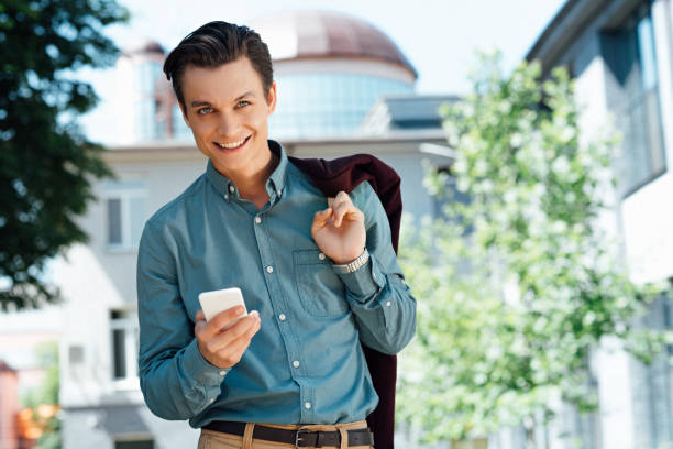 istock handsome young man holding smartphone and smiling at camera 978516792