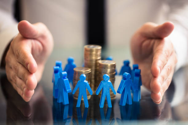 Protecting Blue Human Figures Surrounding Stacked Coins Businessperson's Hand Protecting Blue Human Figures Surrounding Stacked Golden Coins Over Desk crowdfunding stock pictures, royalty-free photos & images