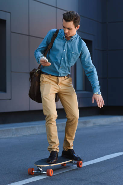 istock handsome young man using smartphone and riding skateboard on street 978525562
