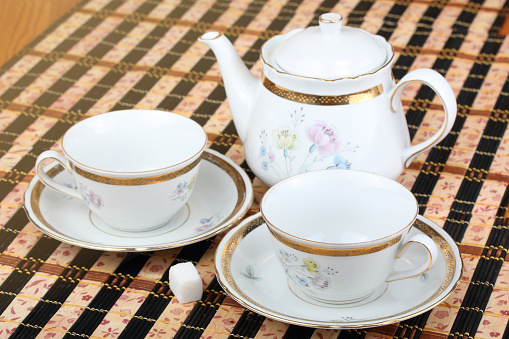 A white and blue china teacup set with a spoon on a wood coffee table with two people sitting in the background.