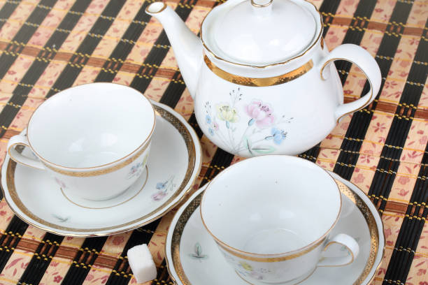 Two empty white porcelain cup and teapot on the table covered with striped bamboo table mat