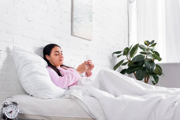 istock smiling woman in pajamas using smartphone while resting in bed at home 978598404