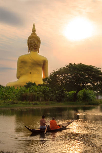 мужчина и монах едут утром на гребной лодке на изображение большого золотого будды в ват муанг (буддийский храм муанг), анг тхонг, таиланд - praying figurine people men стоковые фото и изображения