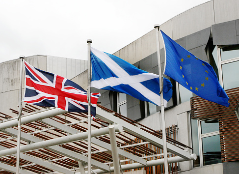 Exterior shot of the Scottish Parliament Building in the Holyrood area of Edinburgh, showing flags of the UK, Scotland, and the European Union. The building houses the devolved Scottish Parliament, and was opened in 2004.