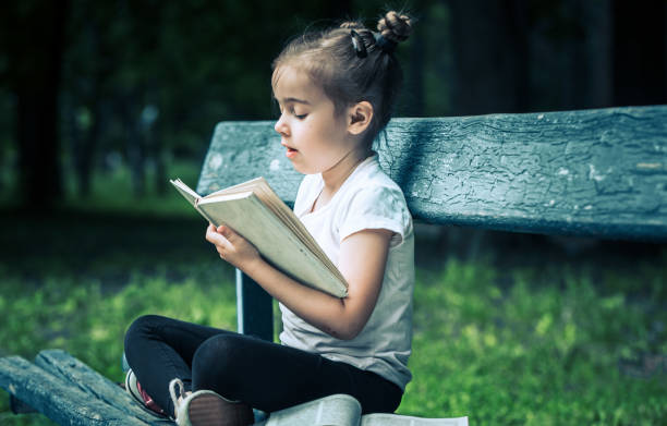 istock little girl is sitting on a bench and is reading a book 978616548