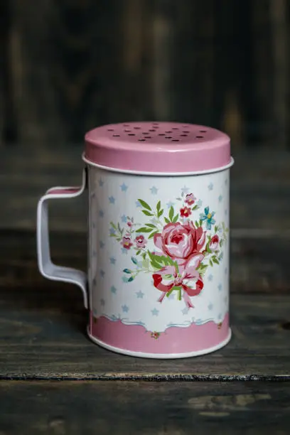 Metal powdered sugar shaker with floral pattern on blue wooden background