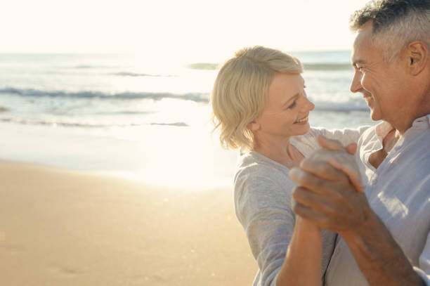 Mature couple dancing on the beach. Mature couple dancing on the beach. They are smiling and having fun. Probably on a romantic vacation. The ocean is in the background middle aged couple dancing stock pictures, royalty-free photos & images