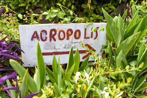 Handmade signpost pointing to the Acropolis in Anafiotika area of Plaka district, Athens, Greece. Plaka and Acropolis are one of the main landmarks of Athens. Vintage sign with an arrow in flowers.