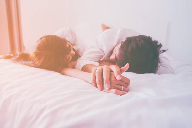 Casal apaixonado, segurando as mãos sono na cama com a luz do sol da manhã - foto de acervo
