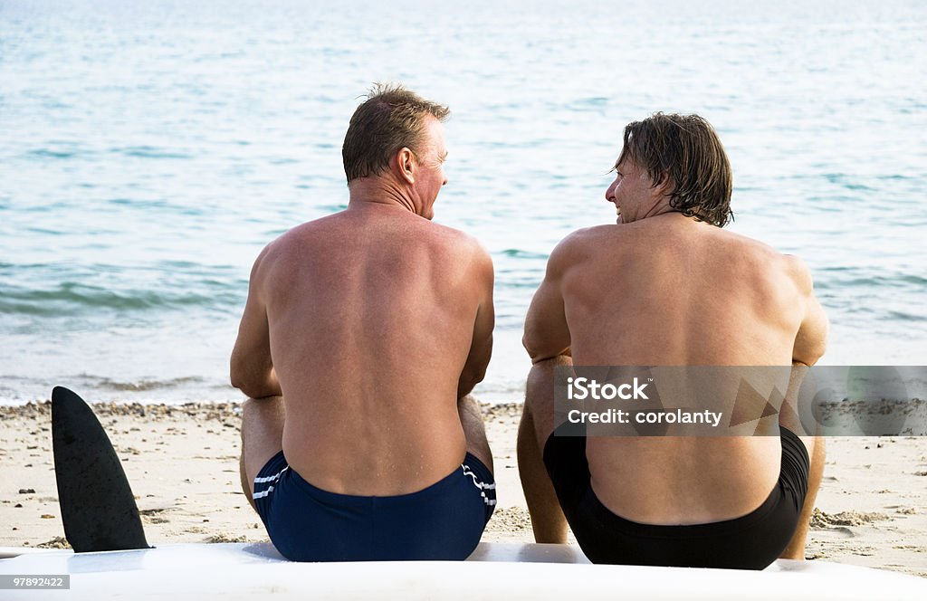 Due uomini seduti insieme sulla spiaggia. - Foto stock royalty-free di 40-44 anni