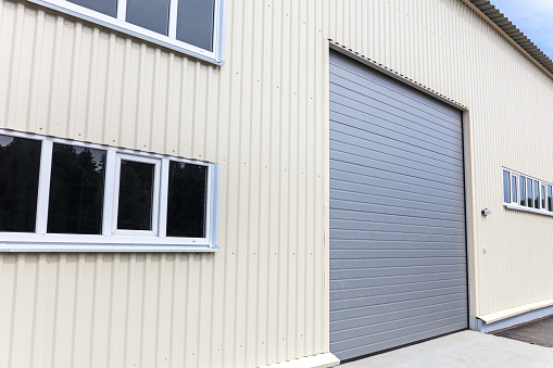 white metal warehouse wall with windows and closed gray gate