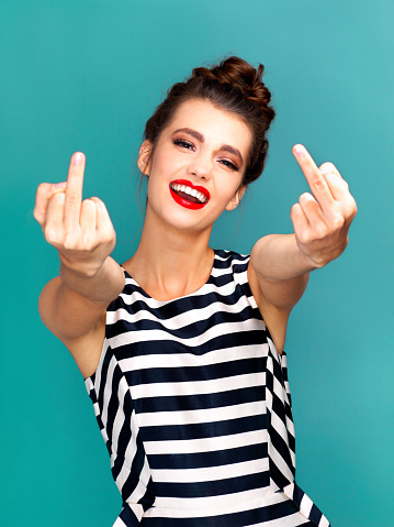 Studio portrait of a beautiful young woman showing the middle finger against a turquoise background