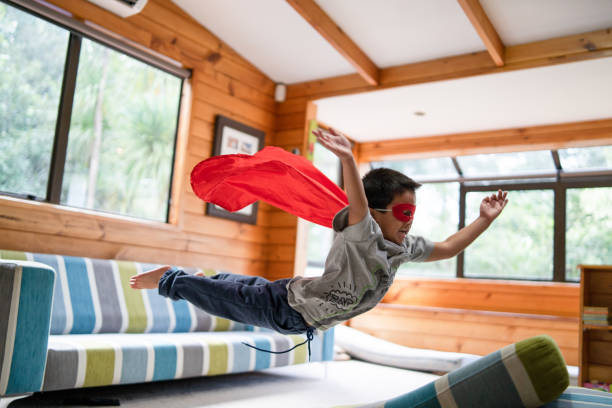 kid avec masque de super-héros sauter sur le canapé. - superhero child creativity little boys photos et images de collection