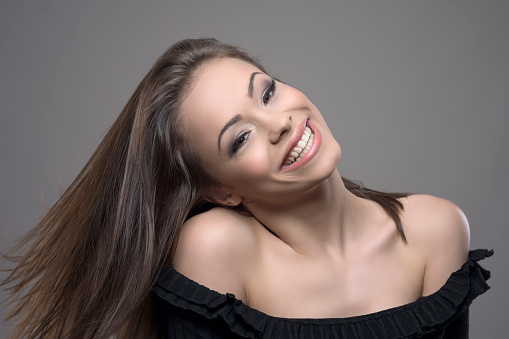 Happy carefree joyful woman with moving flying brown hair smiling and looking at camera over gray studio background.