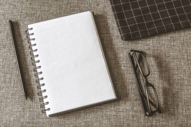 Top view goals list with notebook, pencil, glasses on grey fabric. Flat lay, copy space