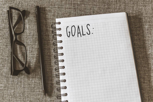 Top view goals list with notebook, pencil, glasses on grey fabric. Flat lay, copy space