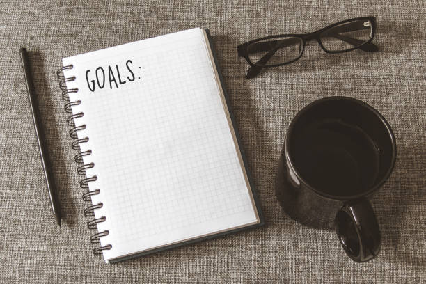 istock Top view goals list with notebook, cup of coffee on grey fabric. Flat lay, copy space 978986012