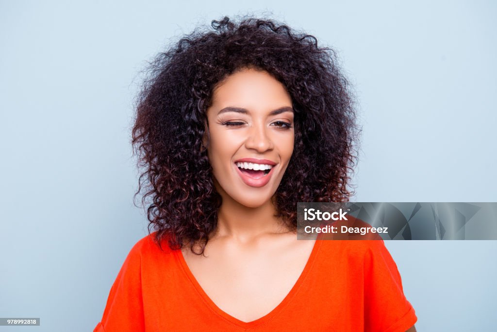 Portrait of cheerful joyful woman in orange outfit with modern hairdo winking with one eye looking at camera isolated on grey background. Affection dream feelings concept Winking Stock Photo