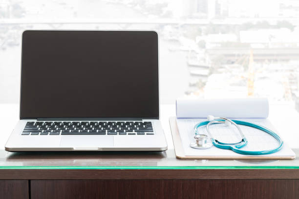 Computer blank screen on doctor's working desk, stethoscope & note pad patients' healthcare record in hospital examination office