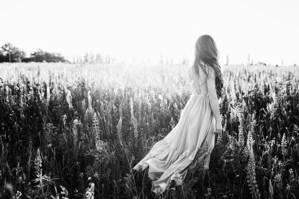 istock Young woman walking on flower field at sunset on background. Horizontal view with copy space 979005688