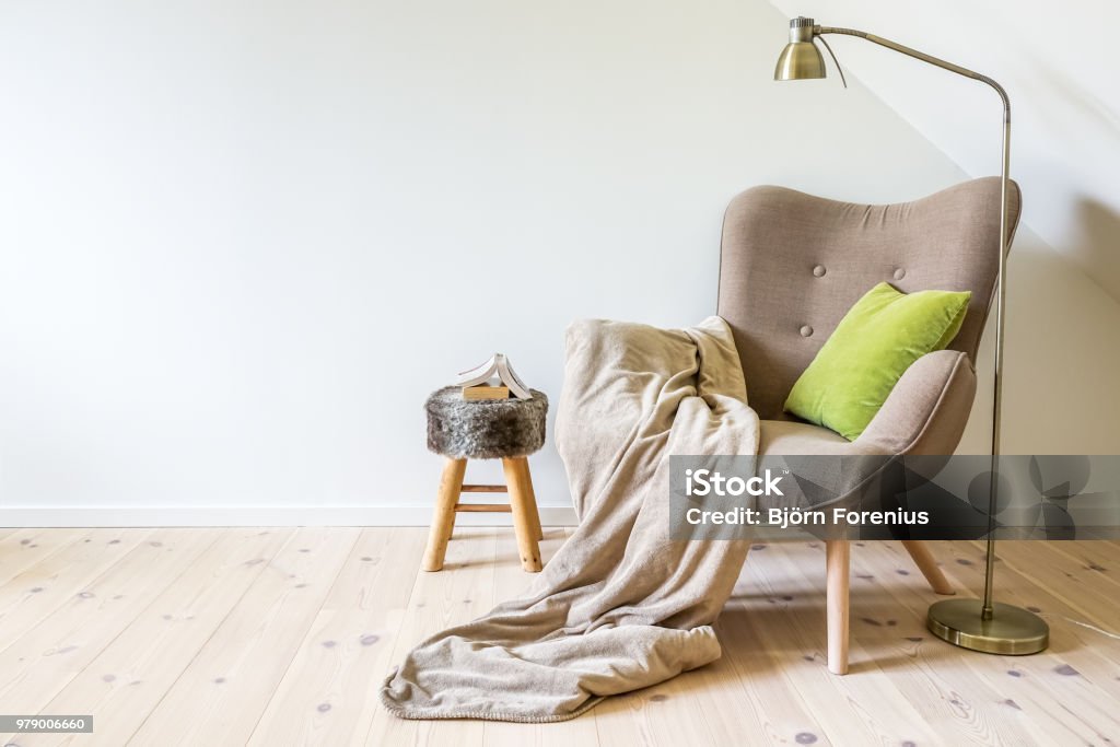 Cozy reading chair A reading chair / armchair with a lamp, blanket and a open book. Empty white wall in simple living room interior. Copy space Armchair Stock Photo