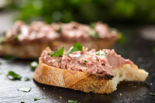 Bitten Liverwurst Sandwich with chopped parsley on a dark slate - close up view