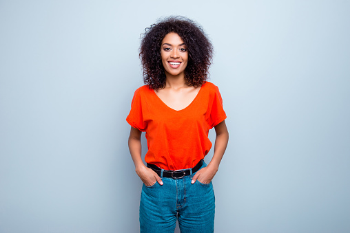 Portrait of joyful cute woman with modern hairdo in bright t-shirt jeans holding two hands in pockets isolated on grey background