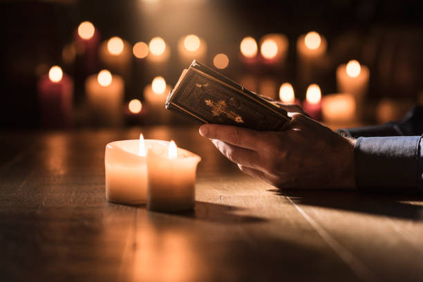 Man reading the Holy Bible and praying in the Church Religious man reading the Holy Bible and praying in the Church with lit candles, religion and faith concept clergy stock pictures, royalty-free photos & images