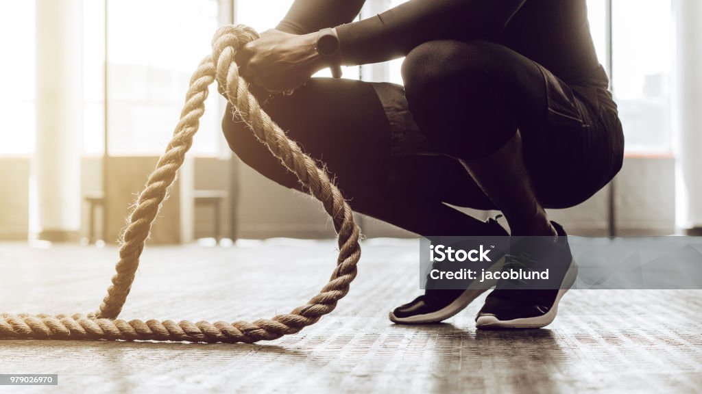 guy training at the gym Close up of a man sitting on his toes holding a pair of battle ropes for workout. guy at the gym working out with fitness rope. Battle Stock Photo