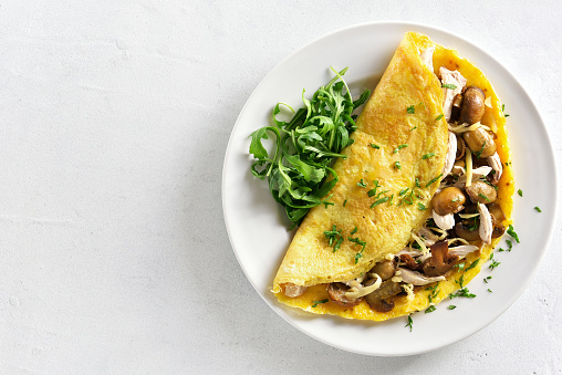 Omelette stuffed with mushrooms, pieces of chicken meat, greens on white stone background with copy space. Top view, flat lay