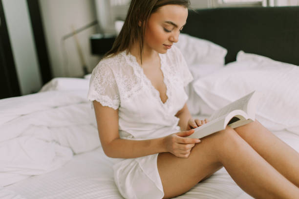 istock Young pretty woman sitting on a bed and reading a book 979032394
