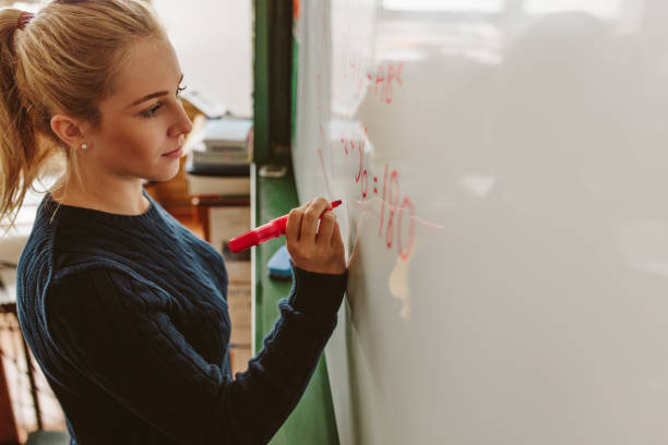 Student writing on board during maths class Close up of female student writing an equation on white board in classroom. Girl writing on board during maths class. writing on chalk board stock pictures, royalty-free photos & images